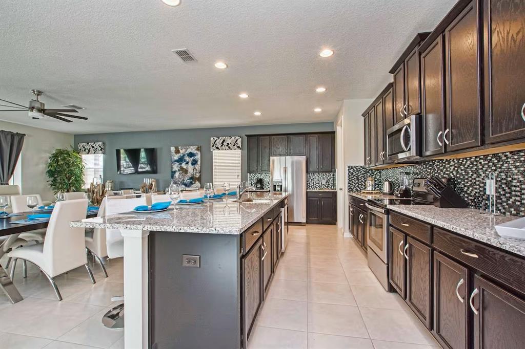 A kitchen with dark wood cabinets, granite countertops, and a large island with bar seating — 9015 SUNSHINE RIDGE LOOP, KISSIMMEE, FL