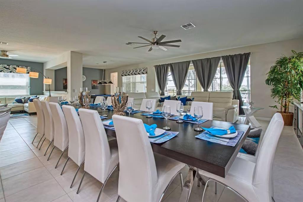 A long dining table with white chairs sits in an open-concept room with tile floors — 9015 SUNSHINE RIDGE LOOP, KISSIMMEE, FL