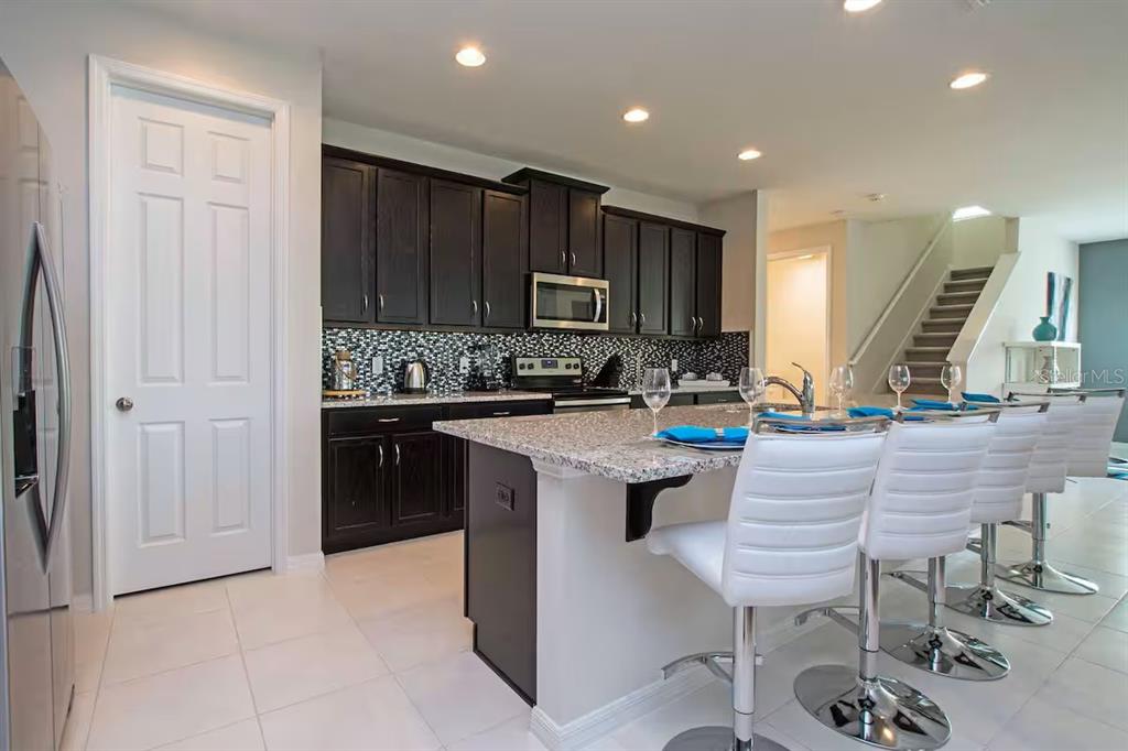 A kitchen with dark wood cabinets, granite countertops, a center island, and white bar stools — 9015 SUNSHINE RIDGE LOOP, KISSIMMEE, FL