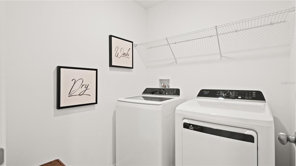 A laundry room features a white washer and dryer with wall-mounted signs and wire shelving — 311 NOLA LANE, DUNDEE, FL
