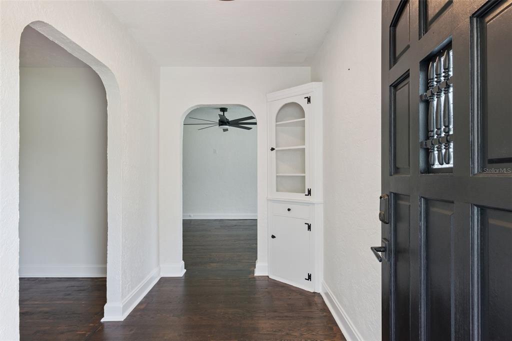 An entryway features dark wood floors, white walls, a black front door, and built-in cabinets — 207 S SUMMERLIN AVENUE, SANFORD, FL