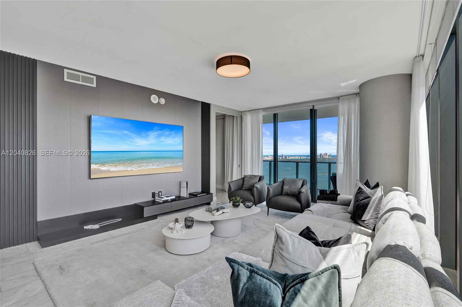 A modern living room features a large wall-mounted television, gray sectional sofa, and floor-to-ceiling windows — 650 NE 32nd St # 3901, Miami FL 33137, MIAMI, FL