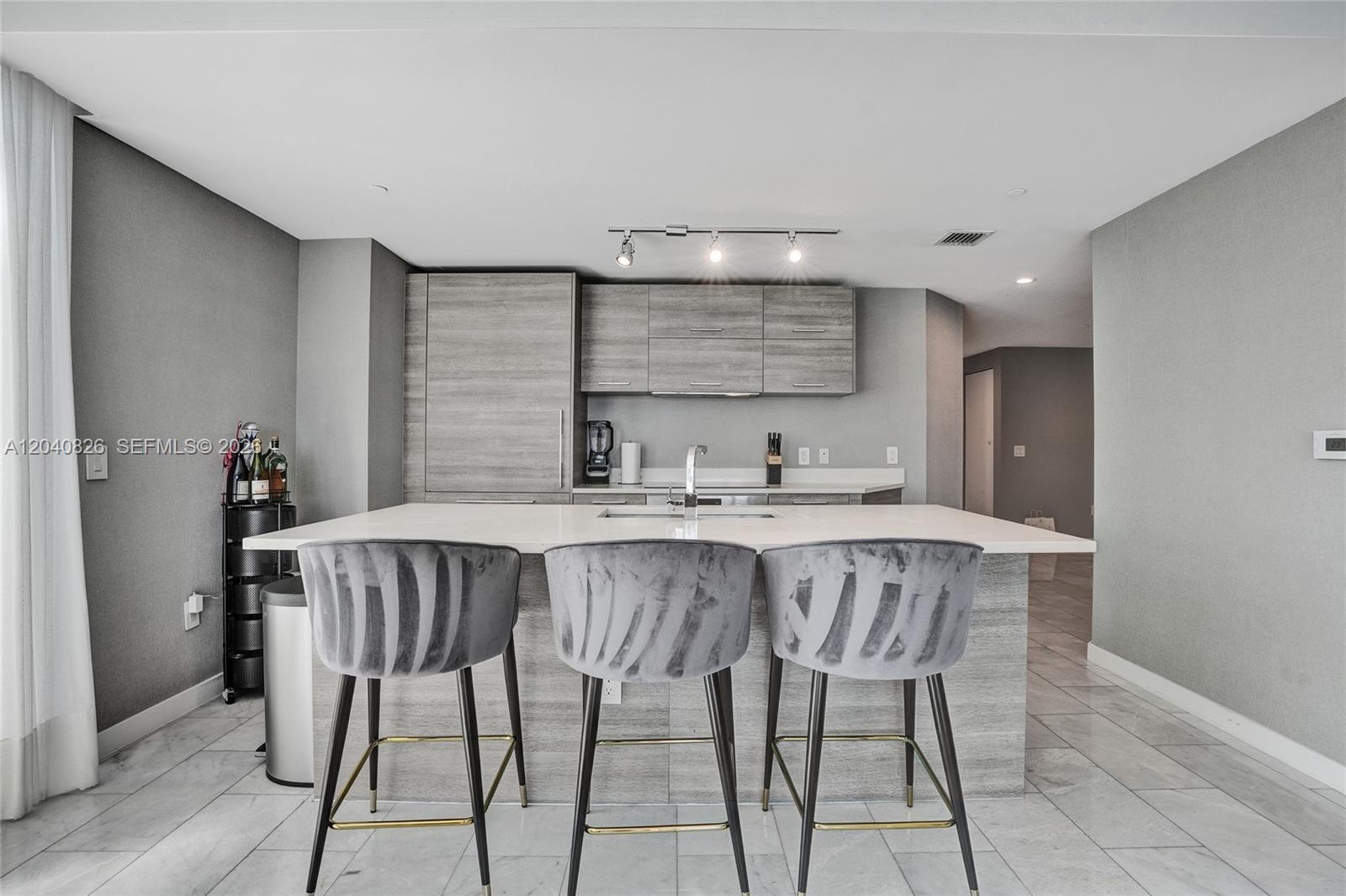 A modern kitchen features gray wood-grain cabinetry, a white island, and three velvet barstools — 650 NE 32nd St # 3901, Miami FL 33137, MIAMI, FL