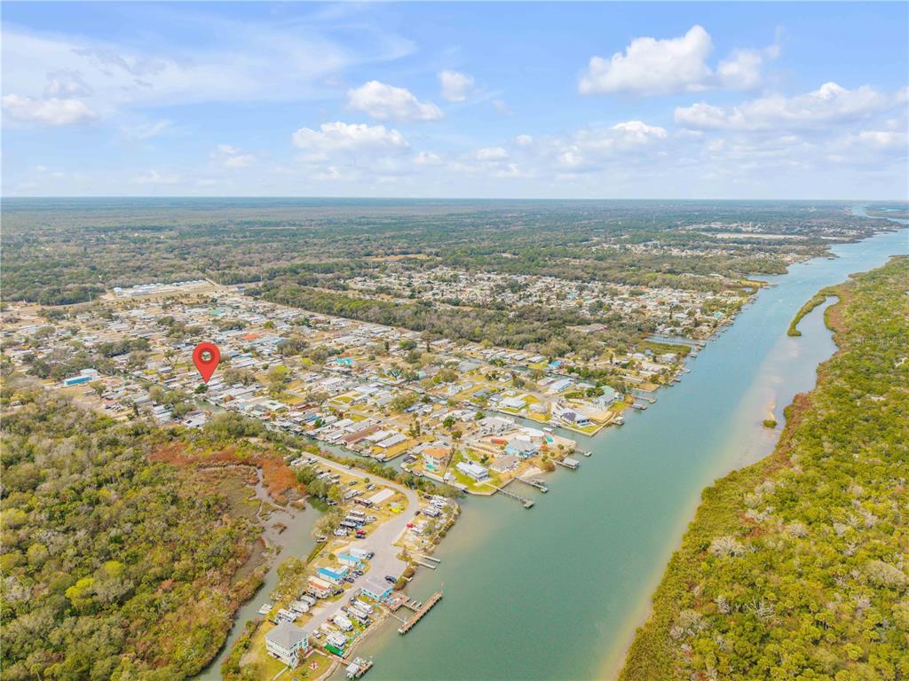 An aerial view shows a residential neighborhood situated along a narrow waterway and surrounding forest — 201 GARY AVENUE, OAK HILL, FL