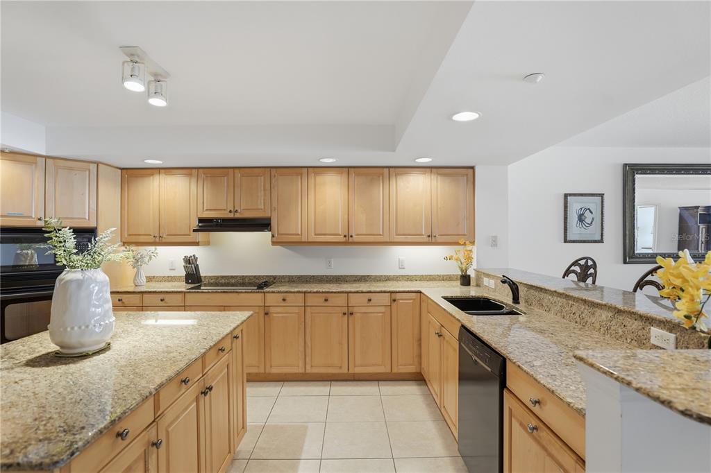A kitchen features light wood cabinets, granite countertops, tile flooring, and black appliances — 16326 GULF BOULEVARD UNIT 307, REDINGTON BEACH, FL
