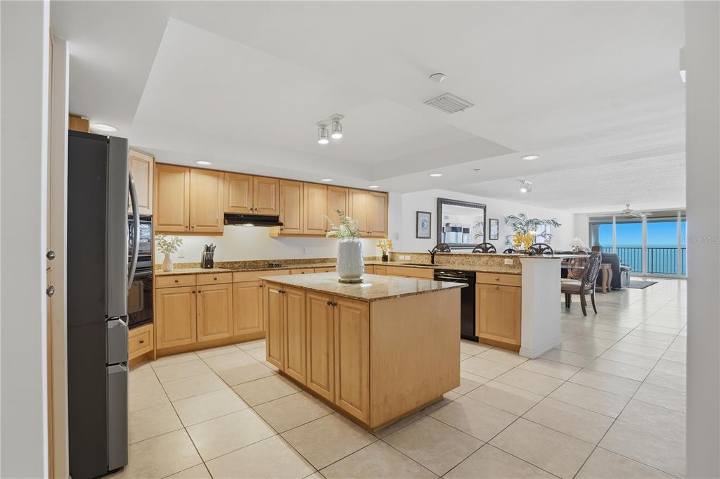 A kitchen with light wood cabinets, granite countertops, and an island overlooks a living area — 16326 GULF BOULEVARD UNIT 307, REDINGTON BEACH, FL