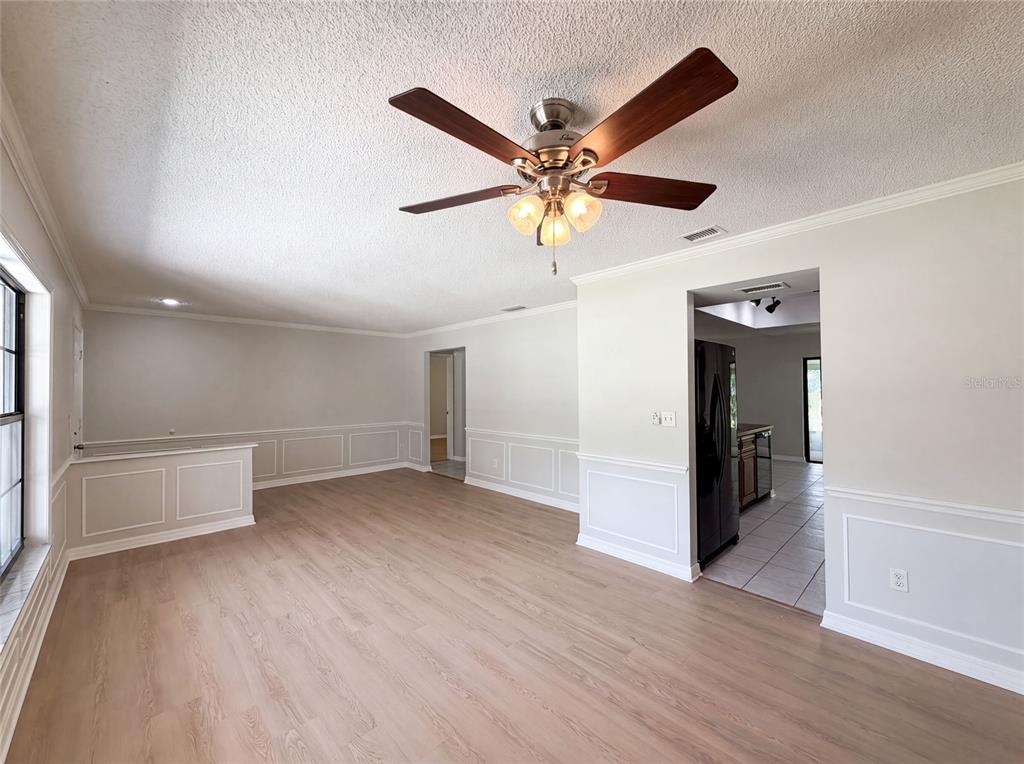An empty living room features light wood-look flooring, white wainscoting, and a ceiling fan — 15226 SW 39TH CIRCLE, OCALA, FL