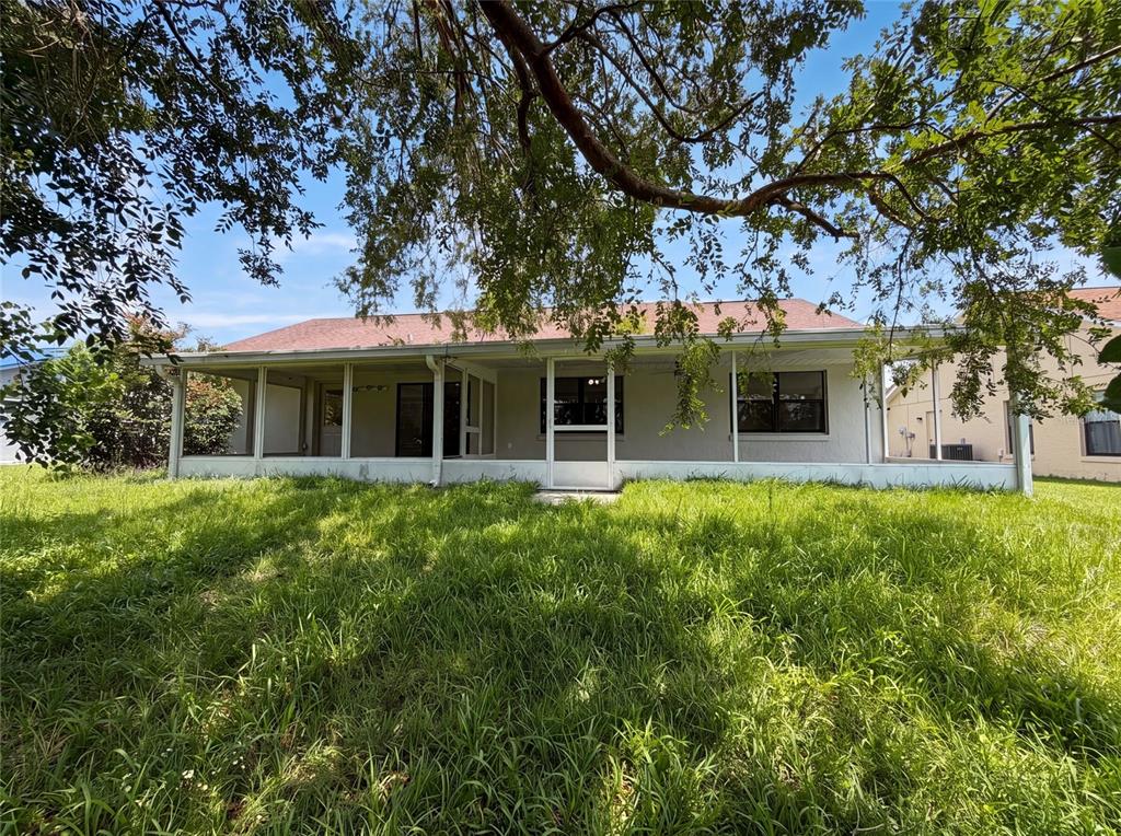 The back exterior of a house features a screened-in porch and an overgrown grassy yard — 15226 SW 39TH CIRCLE, OCALA, FL