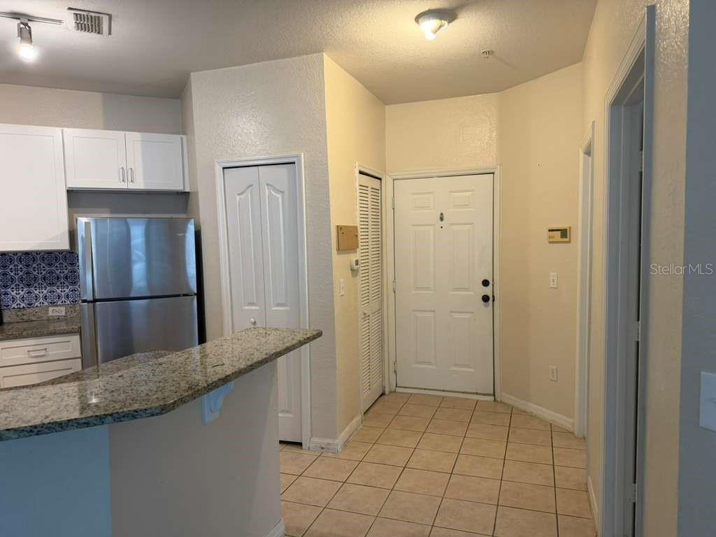 An entryway with tile flooring leads to a kitchen featuring granite countertops and white cabinets — 2639 MAITLAND CROSSING WAY UNIT 107, ORLANDO, FL