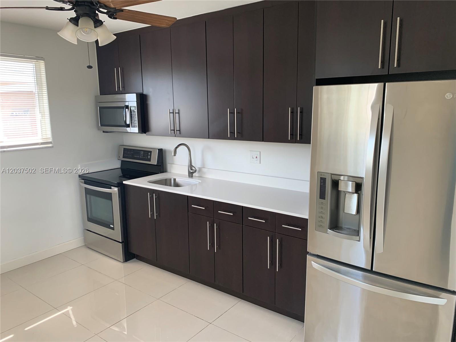 A kitchen features dark wood cabinets, stainless steel appliances, white countertops, and light tile flooring — 1200 SW 31st Ave, Miami FL 33135, MIAMI, FL