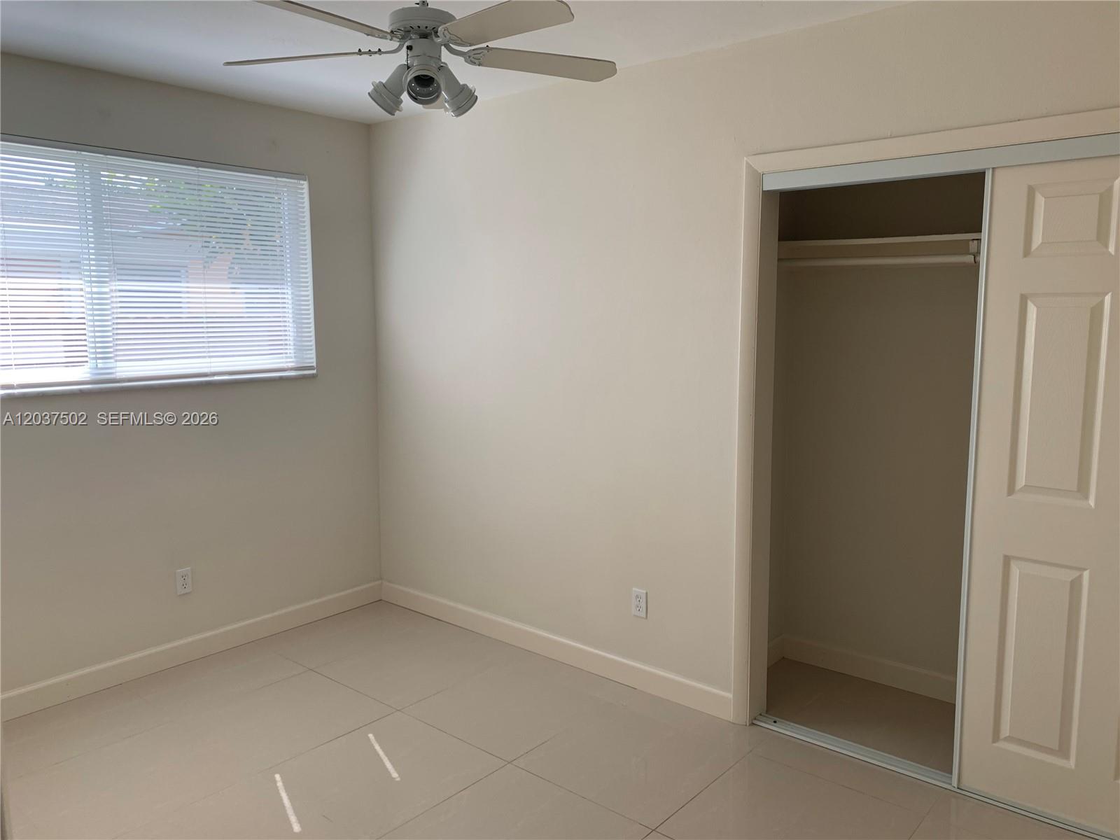 An empty bedroom features light-colored tile flooring, a ceiling fan, a window, and a closet — 1200 SW 31st Ave, Miami FL 33135, MIAMI, FL