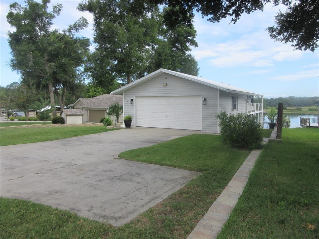 A light gray detached garage with a white door sits on a grassy lakefront lot — 16849 SE 59TH PLACE, OCKLAWAHA, FL