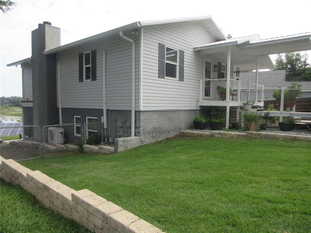 A side view of a house with light gray siding, a chimney, and a covered porch — 16849 SE 59TH PLACE, OCKLAWAHA, FL