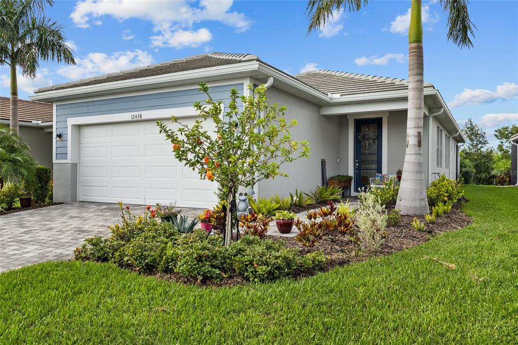 A single-story house exterior features a two-car garage, a front entrance, and landscaped garden beds — 12458 SOMATIC COURT, VENICE, FL