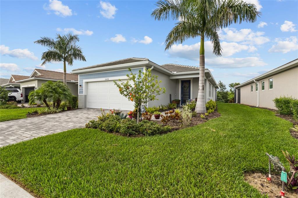 The exterior of a single-story house with a paved driveway, palm trees, and landscaping — 12458 SOMATIC COURT, VENICE, FL