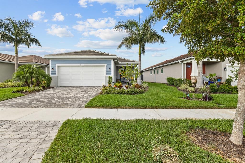A single-story house with a blue facade, white garage door, and palm trees in front — 12458 SOMATIC COURT, VENICE, FL