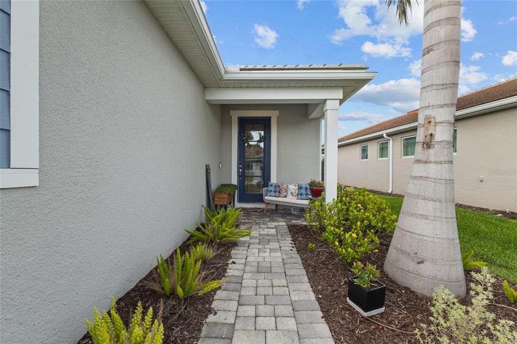 A paved walkway leads to a covered entryway with a blue door and a bench — 12458 SOMATIC COURT, VENICE, FL
