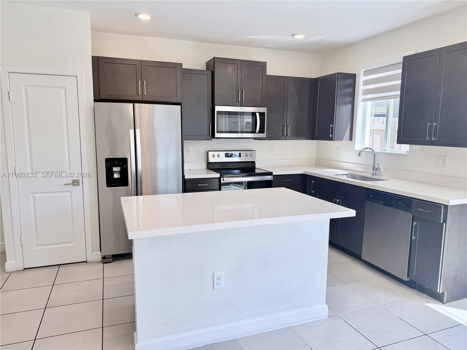 A kitchen features dark cabinets, stainless steel appliances, a white island, and light tile flooring — 2418 SE 10th Ct, Homestead FL 33035, HOMESTEAD, FL