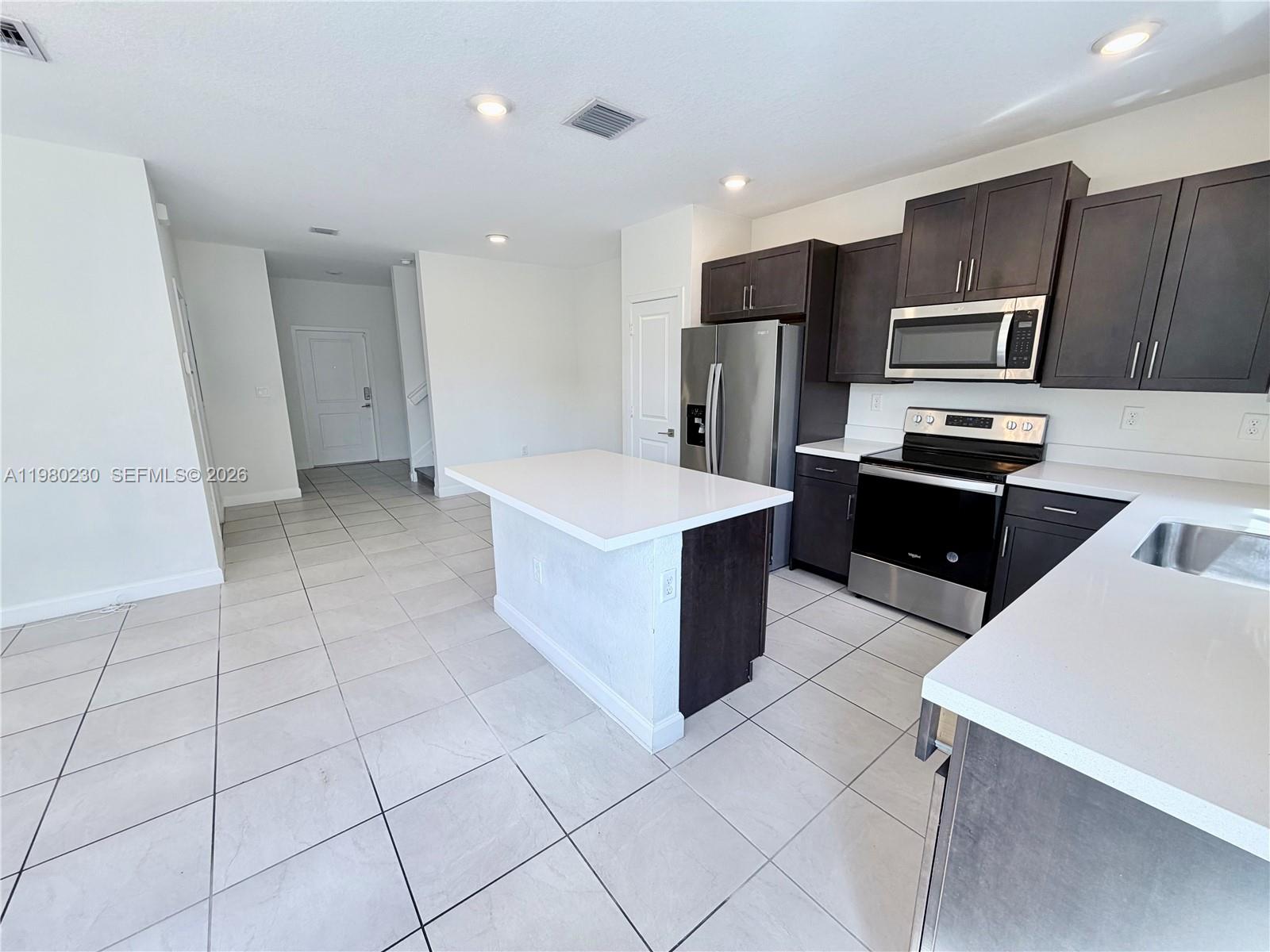 A kitchen features dark cabinets, stainless steel appliances, a white island, and light tile flooring — 2418 SE 10th Ct, Homestead FL 33035, HOMESTEAD, FL