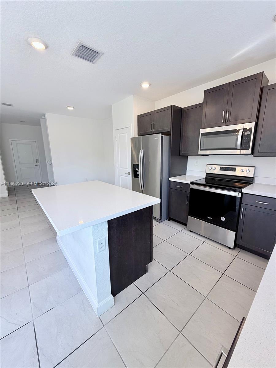 A modern kitchen features dark cabinetry, stainless steel appliances, and a white quartz island — 2418 SE 10th Ct, Homestead FL 33035, HOMESTEAD, FL
