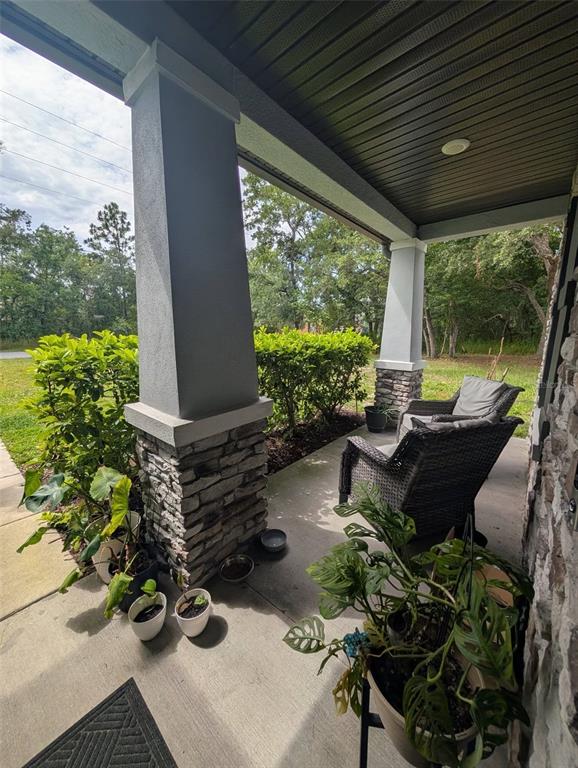 A covered front porch features stone-based columns, wicker chairs, and several potted plants — 12076 MARVELWOOD ROAD, WEEKI WACHEE, FL