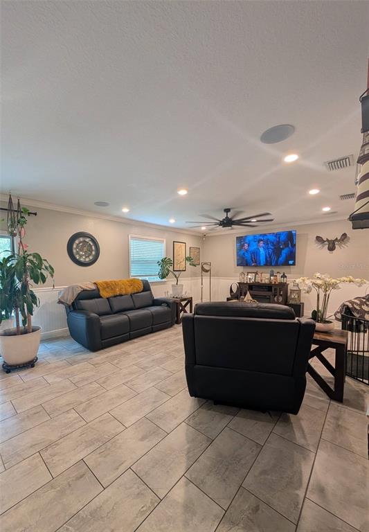A living room features tile flooring, a black sofa, a recliner, and a wall-mounted television — 12076 MARVELWOOD ROAD, WEEKI WACHEE, FL