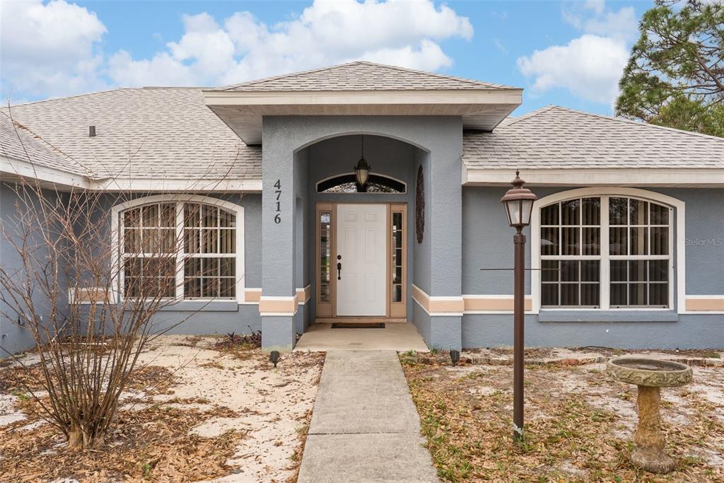 A gray single-story house features a white front door, arched entryway, and two large windows — 4716 BOABADILLA AVENUE, SEBRING, FL