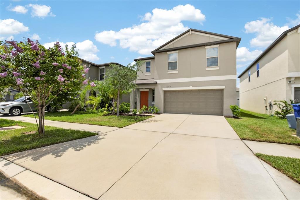 A two-story suburban house features a tan exterior, a two-car garage, and a concrete driveway — 4907 WILD SENNA BOULEVARD, TAMPA, FL