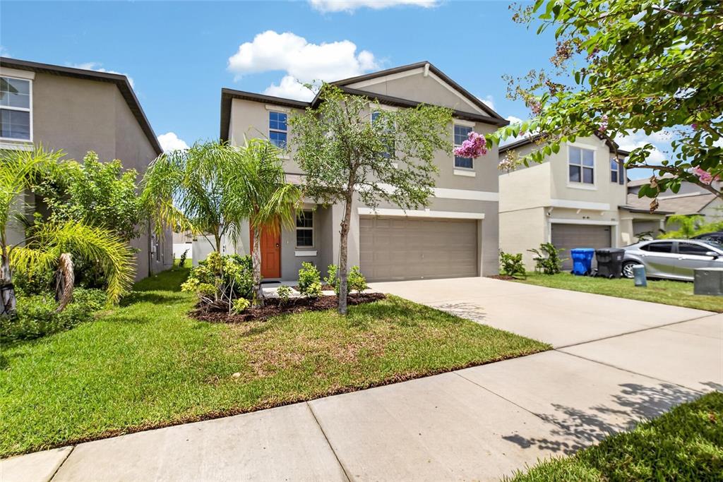 A two-story suburban house with a tan exterior, orange front door, and a concrete driveway — 4907 WILD SENNA BOULEVARD, TAMPA, FL
