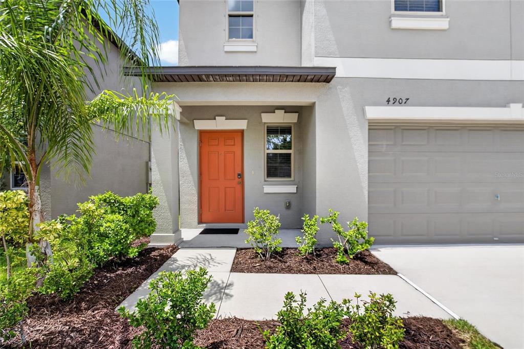 The exterior of a two-story house features a gray facade, an orange door, and landscaping — 4907 WILD SENNA BOULEVARD, TAMPA, FL