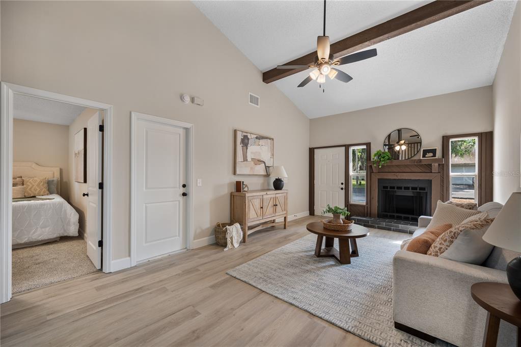 A living room with a vaulted ceiling, fireplace, wood-look flooring, and an adjacent bedroom doorway — 265 LAKE THOMAS DRIVE, WINTER HAVEN, FL