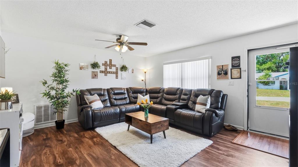 A living room features a dark leather sectional sofa, a coffee table, and wood-look flooring — 7020 ASHMONT AVENUE, BROOKSVILLE, FL