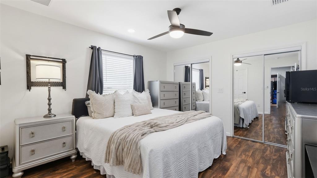 A bedroom features a bed with white bedding, mirrored closet doors, and wood-look flooring — 7020 ASHMONT AVENUE, BROOKSVILLE, FL