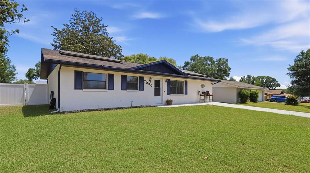 A single-story house with white stucco walls, dark blue shutters, and a large front lawn — 7020 ASHMONT AVENUE, BROOKSVILLE, FL