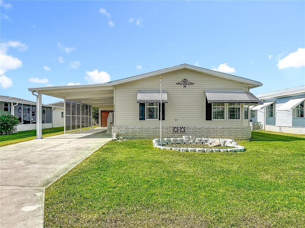 A single-story mobile home with beige siding, a carport, and a stone-bordered garden bed — 5745 PAWNEE STREET, ZEPHYRHILLS, FL