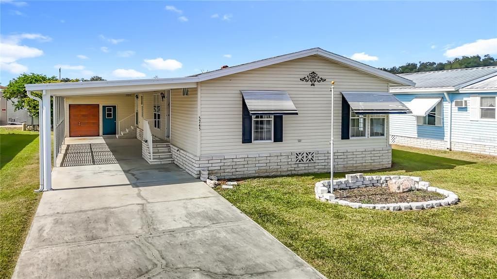 A single-story manufactured home features light siding, a concrete driveway, and a covered carport — 5745 PAWNEE STREET, ZEPHYRHILLS, FL