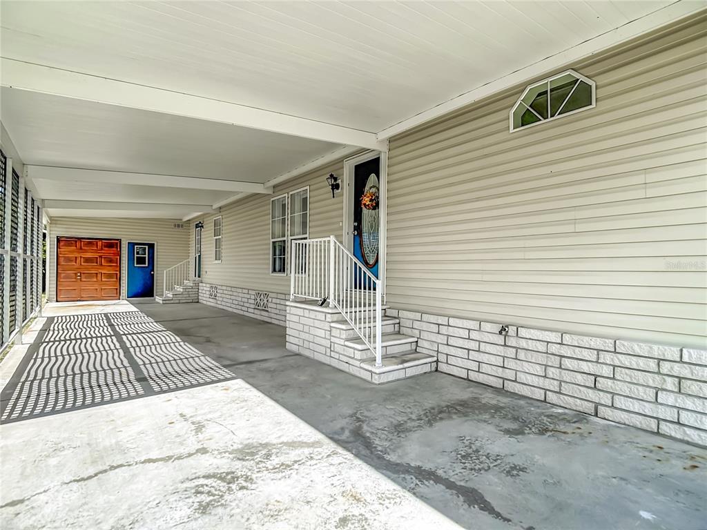 A covered concrete carport leads to a house entrance with white brick steps and siding — 5745 PAWNEE STREET, ZEPHYRHILLS, FL