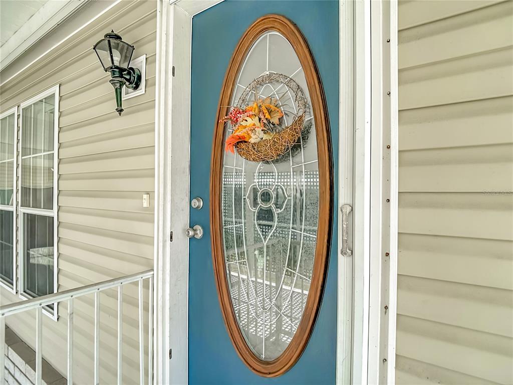 A blue front door with an oval glass insert and a wreath sits on a porch — 5745 PAWNEE STREET, ZEPHYRHILLS, FL