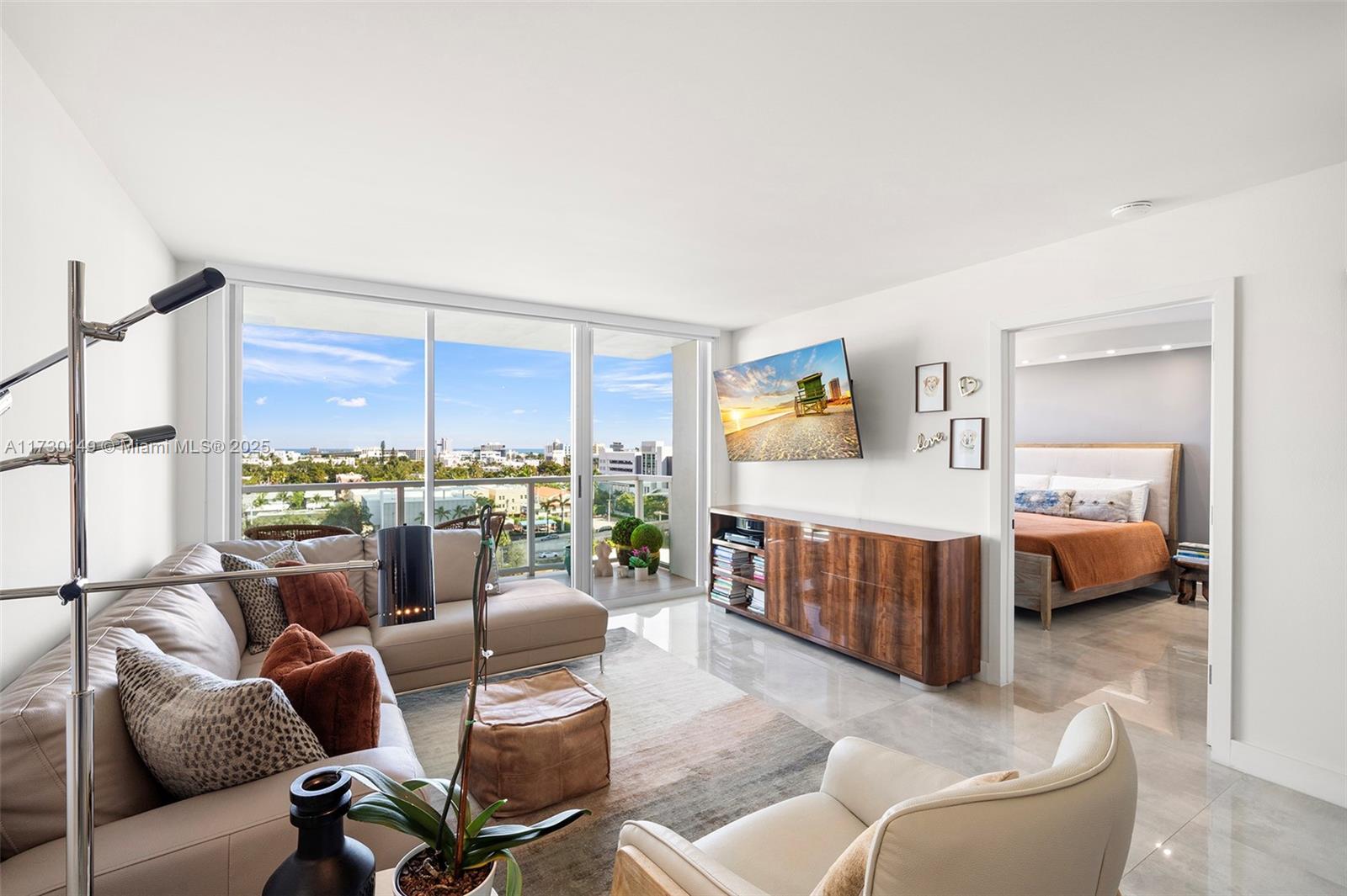 A modern living room features a beige sectional, wood media console, and floor-to-ceiling balcony windows — 650 West Ave # 1004, Miami Beach FL 33139, MIAMI BEACH, FL