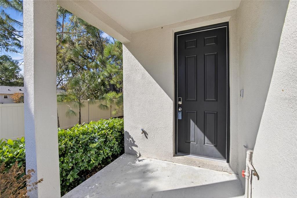 A covered concrete porch features a dark gray front door and a white stucco wall — 2710 SCARLET BAY PLACE, BRANDON, FL