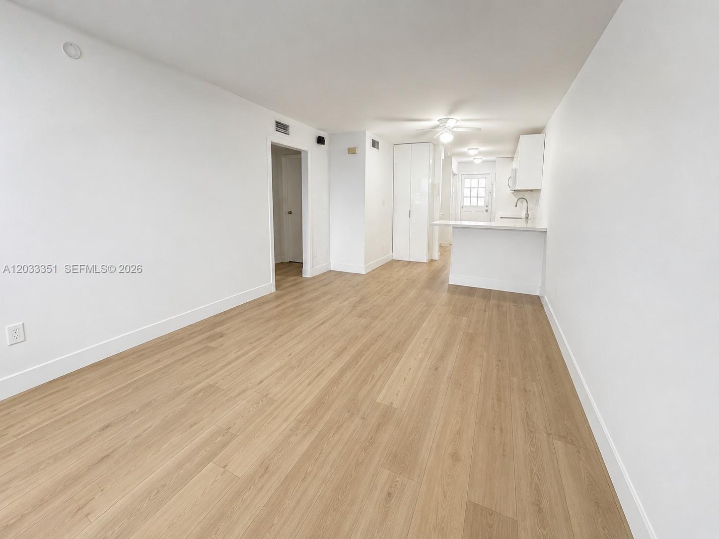 An open-concept living area features light wood-look flooring, white walls, and a small kitchen — 301 Bonaventure Blvd # 7, Weston FL 33326, WESTON, FL