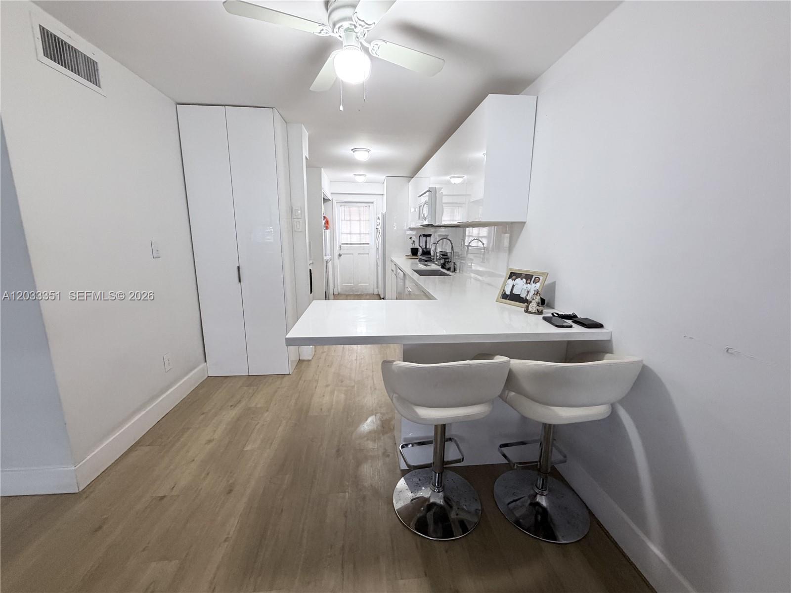 A modern kitchen features white cabinetry, a breakfast bar with two stools, and wood flooring — 301 Bonaventure Blvd # 7, Weston FL 33326, WESTON, FL