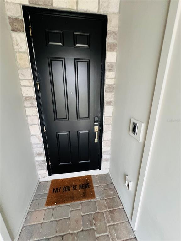 A black front door with a stone surround and a welcome mat on a paved entryway — 11258 WHISTLING PINE WAY, ORLANDO, FL