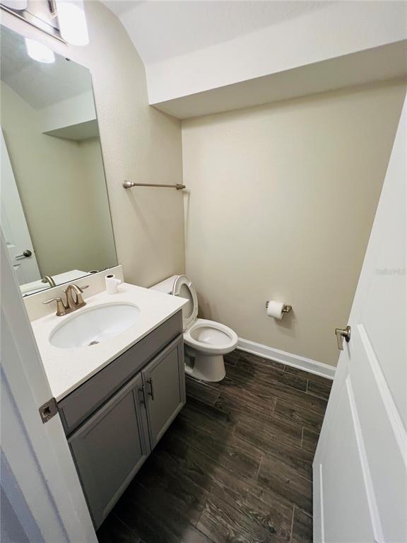 A small bathroom features a gray vanity, white countertop, toilet, and dark wood-look flooring — 11258 WHISTLING PINE WAY, ORLANDO, FL