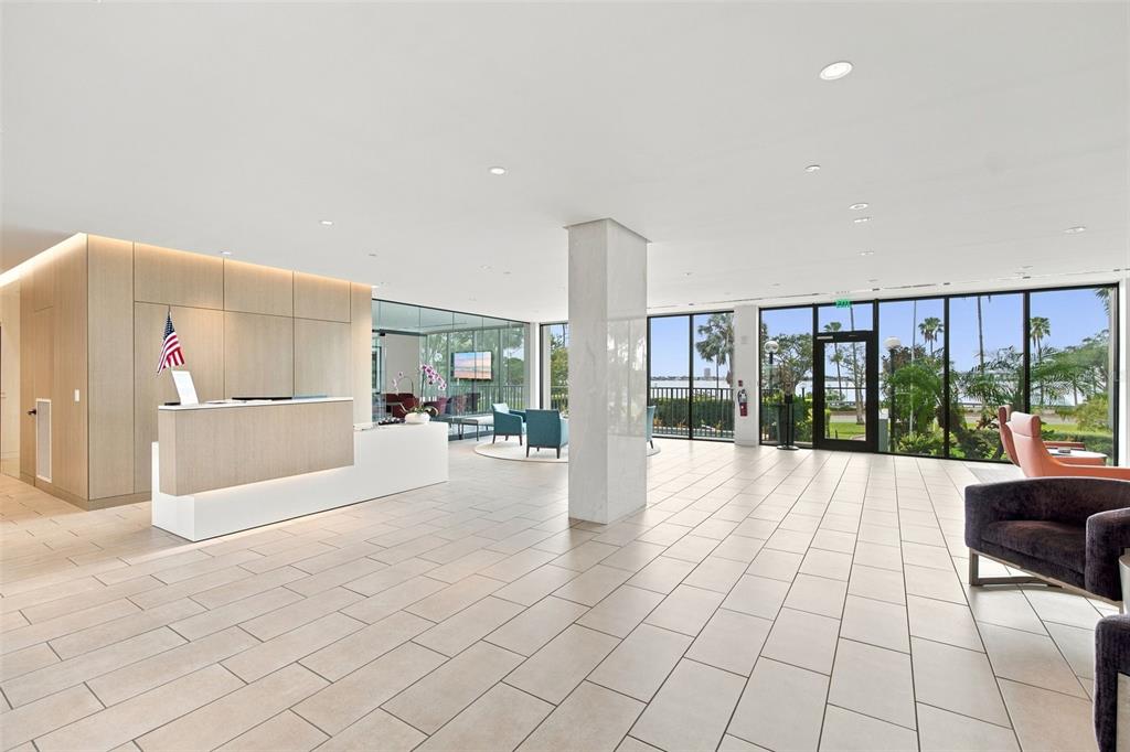 A modern lobby features a reception desk, tile flooring, and floor-to-ceiling windows overlooking palm trees — 770 S PALM AVENUE UNIT 1804, SARASOTA, FL