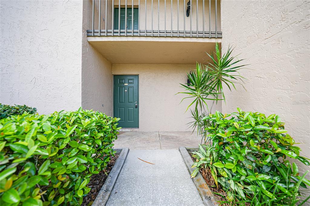 A concrete walkway leads to a green front door beneath a second-story balcony — 601 SHREVE STREET UNIT 51A, PUNTA GORDA, FL