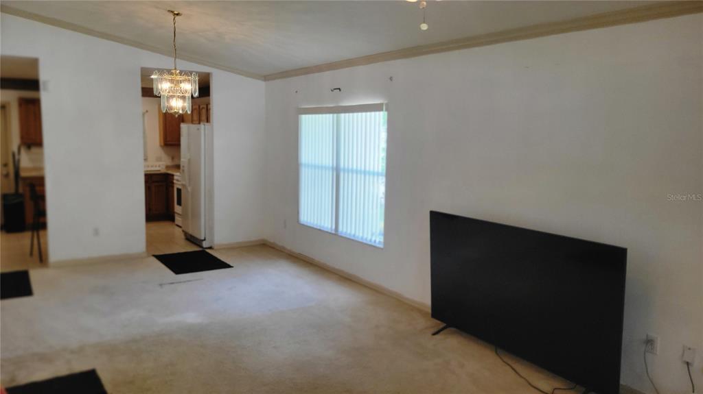 A living room with beige carpet, white walls, a large television, and a crystal chandelier — 1517 NE 40TH PLACE, GAINESVILLE, FL