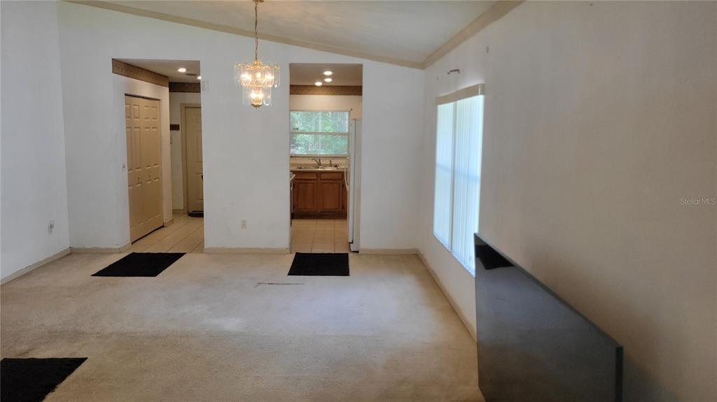 A living room with beige carpet, white walls, a chandelier, and an adjacent kitchen — 1517 NE 40TH PLACE, GAINESVILLE, FL