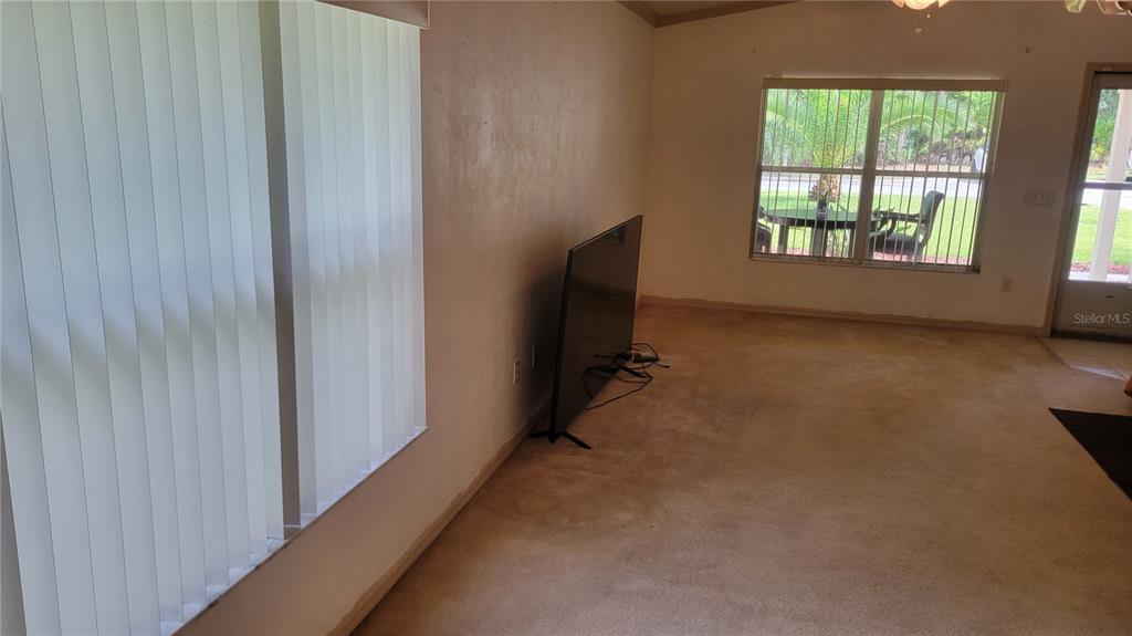 A living room features beige carpeting, a television on a stand, and a large window — 1517 NE 40TH PLACE, GAINESVILLE, FL