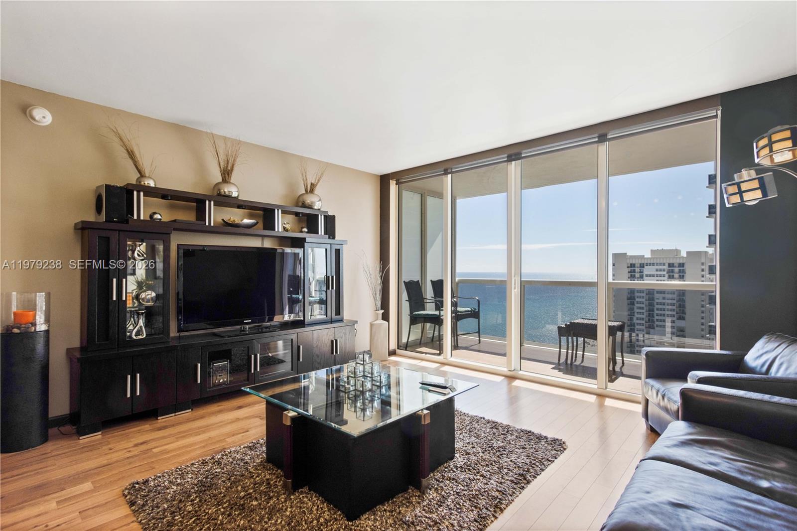 A living room features a dark entertainment center, glass coffee table, and floor-to-ceiling ocean views — 1830 S Ocean Dr # 2105, Hallandale Beach FL 33009, HALLANDALE BEACH, FL